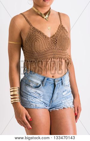 Closeup of female model's body in brown crochet fringes crop top and denim shorts. No retouch
