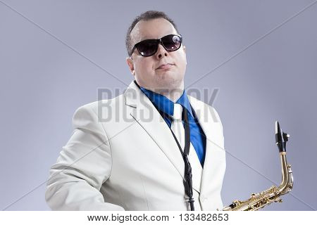Music Concept and Ideas. Handsome Caucasian Musician with Alto Saxophone Posing in White Siut Against Gray. Horizontal Image