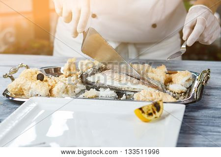Hand with spatula cutting fish. Tray with cooked fish. Dorado fish prepared by chef. Seafood delicacy in restaurant kitchen.