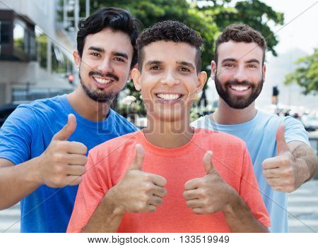 Three latin and caucasian friends showing thumb up outside in the city in the summer