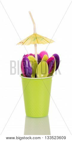 Green colored disposable cup with plastic spoon and an umbrella isolated on white background.