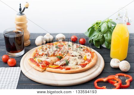 Italian pizza with cherry tomatoes pepper salami and basil on the wooden background. Rustic style.