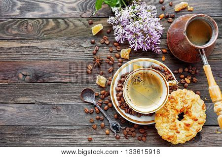 Rustic wooden background with cup and cezve of coffee peanut tart and lilac flowers. White vintage dinnerware and spoon. Breakfast at summer morning. Top view place for text.
