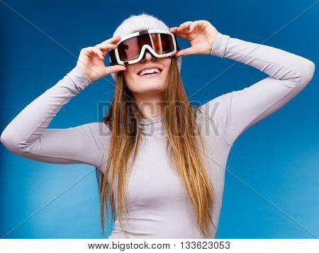 Attractive woman in winter cap gray sports thermal underwear for skiing training ski googles studio shot on blue.