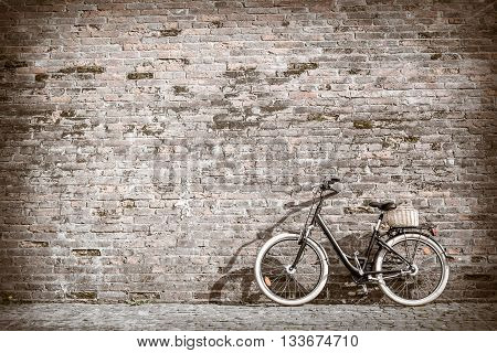 Black retro vintage bicycle with old brick wall and copy space. Retro bicycle with basket in front of the old brick wall. Old photo effect applied. Toned.