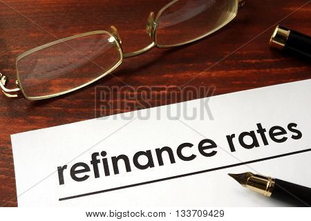 Paper with words refinance rates on a wooden background.