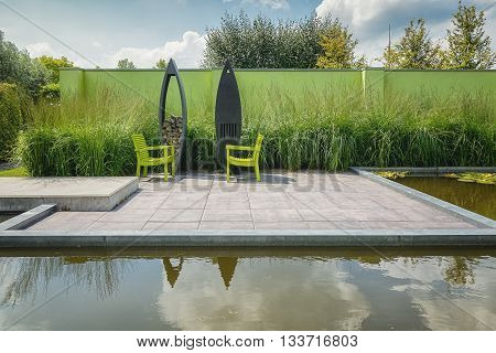 Appeltern, The Netherlands - July 22, 2015: The Gardens of Appeltern is the inspiration garden park in the Netherlands. In this picture 2 green chairs with with a modern outdoor fireplace and storage firewood.