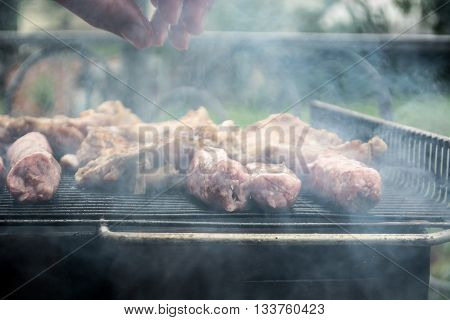 Grilling cevapi and pork chops. Putting raw meat on grill