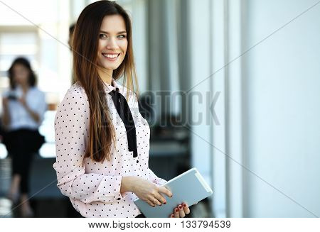 Business woman standing in foreground with a tablet in her hands, her co-workers discussing business matters in the background