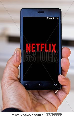 SPAIN - 13 MARCH 2016: Close-up of man's hand holding cell with netflix logo on screen. Netflix is an international leading subscription service for watching TV episodes and movies.