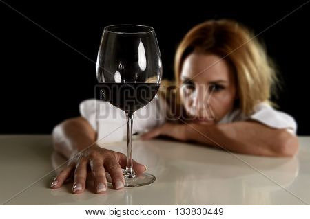 drunk blond woman alone in wasted depressed expression looking thoughtful and sad holding red wine glass isolated on black background in alcohol abuse and alcoholic housewife concept