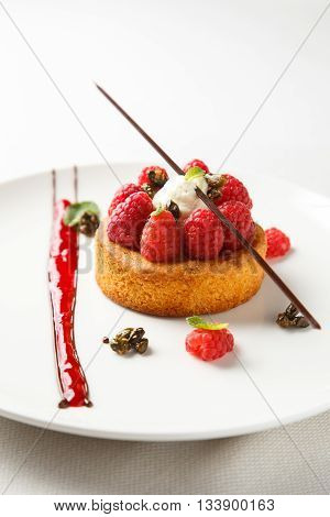Sable breton or Breton shortbread with vanilla cream and raspberry coulis on white dish.