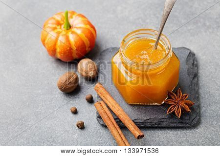 Pumpkin confiture jam sauce with spices on stone table.