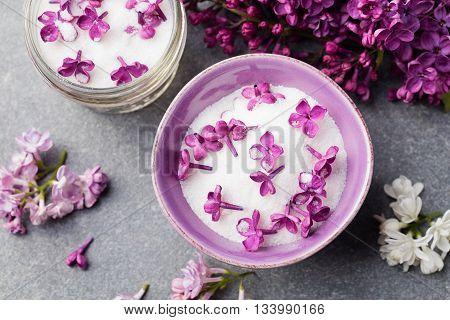 Lilac flowers sugar and syrup essential oil with flower blossoms in glass jar Grey stone background Top view.