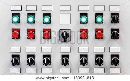 Control panel of industrial equipment with name plates switches red buttons and glowing green buttons