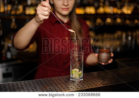 Female Bartender Pourring A Spoon Of Cane Sugar Into A Glass At The Steel Bar Counter
