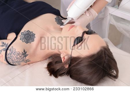 Cosmetologist with patient and professional tattoo removal laser in salon