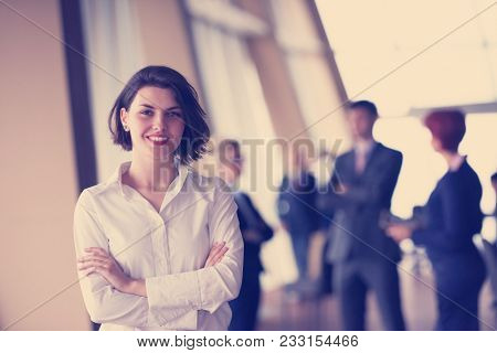 Smilling young business woman in front her team blured in background. Group of young business people. Modern bright  startup office interior.