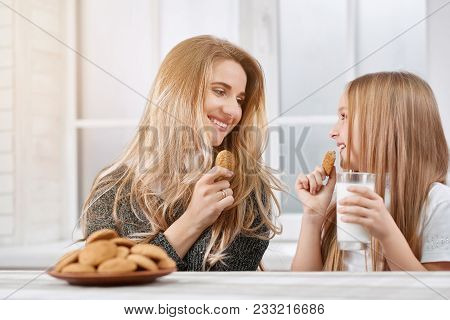 Portarait Of Older And Younger Sisters Eating Cookies And Smile.