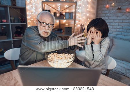 Grandfather And Grandson Are Watching Scary Movie At Table At Night At Home.