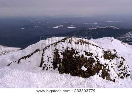View From A Snow-capped Mountain Pass With A Boulder Covered With Lichen Protruding From Under Firn 