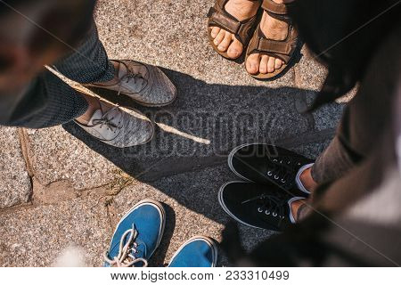 Top View Of Friends Shoes On Road. Legs Of Group Of People In City Street In Sunny Day. Summer Vacti