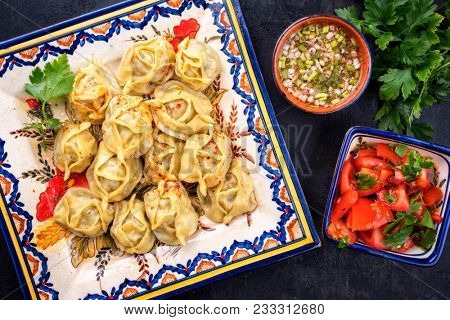 Traditional uzbek manti steamed with minceed meat and tomato paprika salad as top view on a plate 
