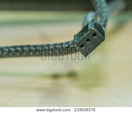 Closeup Of Black Three Pin Electrical Computer Connector With Braided Wire Covering Blurred Out In B