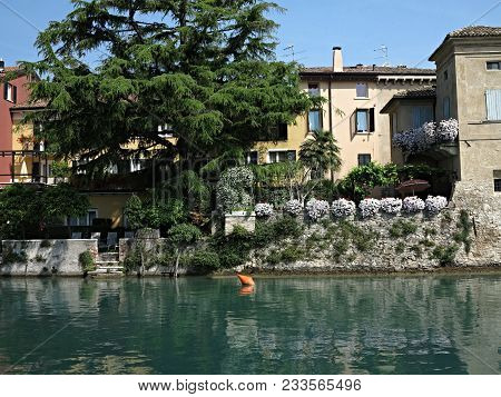 Emerald Smooth Surface Of Lake Garda At The Walls Of The Resort Town.