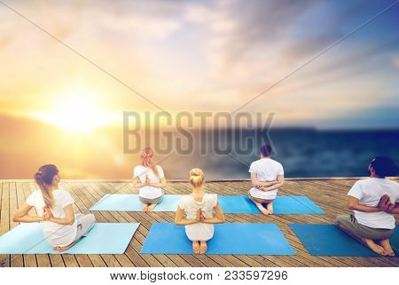 fitness and healthy lifestyle concept - group of people doing yoga reverse prayer pose on wooden pier over sea background