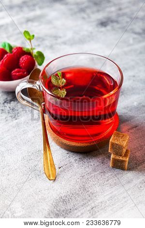 Hot Raspberry Tea In Transparent Cup On A Stone Table. Fresh Berries, Cubes Of Cane Sugar And A Bag 