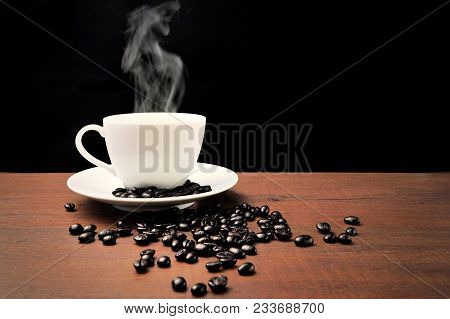 Hot White Coffee Cup And Coffee Beans And Steam On The Wooden Table And Black Background.copy Space 