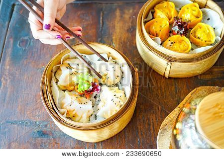 Prawn gluten free dumplings. Chicken curry steamed dumpling. A hand with chopsticks holds a piece. Wooden table background in a restaurant. Traditional Chinese cuisine. Top view with copy space.