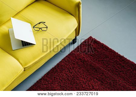 Half-closed Laptop And Eyeglasses On Yellow Leather Couch