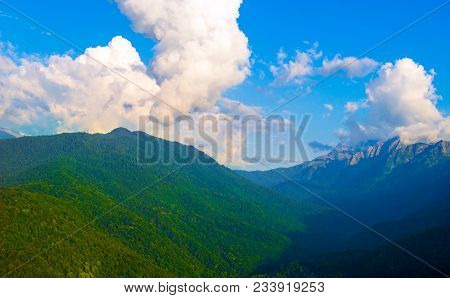 Fluffy Cumulus Clouds In The Mountains Against The Blue Clear Sky