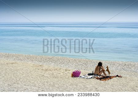 Varigotti, Liguria, Italy - May 21, 2009: Sunbathing Woman And Her Little Dog At Varigotti Beach On 