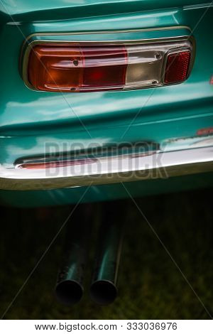 Close Up Vertical Image Of The Red Tail Light And Exhaust Pipes Of A Green Classical Vintage Car.