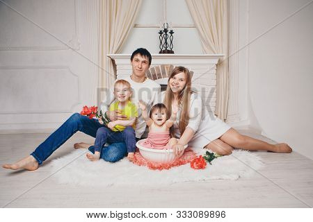 A Little Girl With Family Is Bathing In A Bath With Flowers By The Fireplace. A Child Washes In A Ba