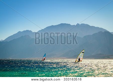 Surfers Ride In The Sea On The Background Of The Rocky Coast In Egypt Dahab