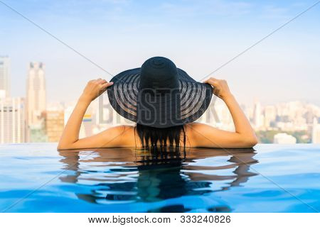 Young woman in a roof top swimming pool, infinity pool with beautiful city view. Vacation in Singapore.