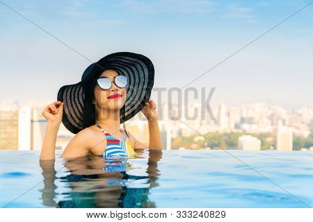 Young woman in a roof top swimming pool, infinity pool with beautiful city view. Vacation in Singapore.