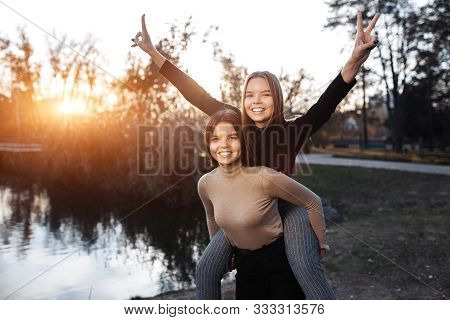 Positive Two Young Twin Sisters In Casual Outfit With Bright Smile Posing At The Park. Freedom Conce