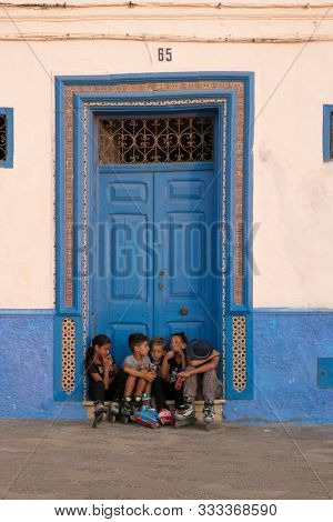 Asilah, Morocco-September 10, 2019: Children sitting in front of a blue painted wooden door in the medina of Asilah, Morocco