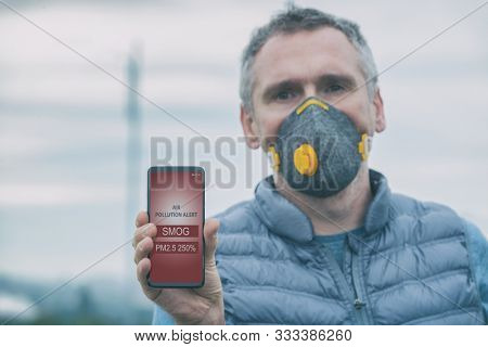 Man wearing a real anti-pollution, anti-smog and viruses face mask and checking current air pollution with smart phone app