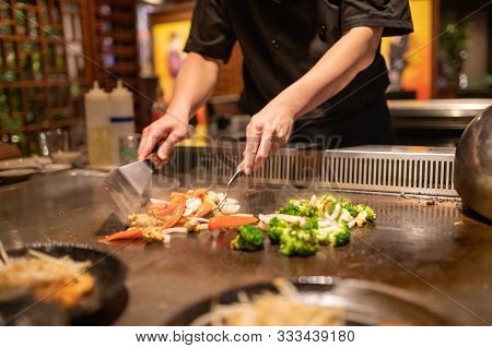 Teppanyaki Chef Preparing Japanese Cuisine On Hot Metal Plate By Cutting Up Vegetables