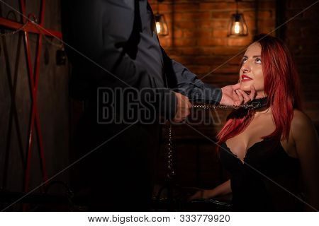 Leather Belt On The Neck Of Bdsm. Luxurious Chest In Black Underwear. A Woman Kneels In Front Of Her