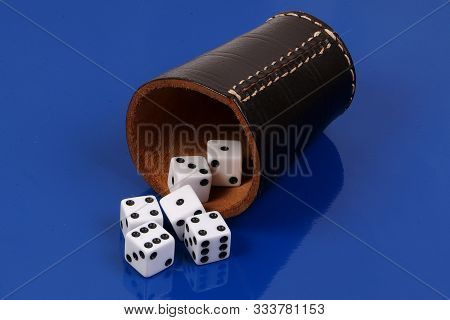 White Dice Falling From A Recumbent Leather Dice Cup On A Blue Background