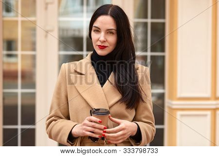 Horizontal Image Of Serious Confident Businesswoman Holding Papercup Of Coffee, Looking Directly At 