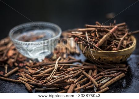 Manjistha Powder And Its Roots On Black Wooden Surface Along With Some Lukewarm Water In A Glass Bow