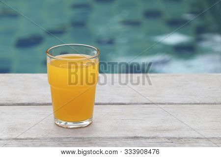 Glass Of Orange Juice Placed On A Wooden Floor By The Pool.